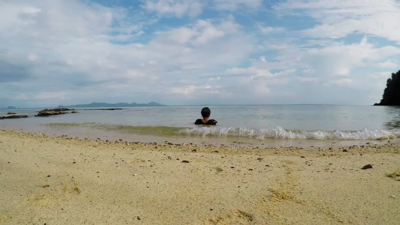 Caucasian woman sits in the water and watches horizon- low angle shot from behind