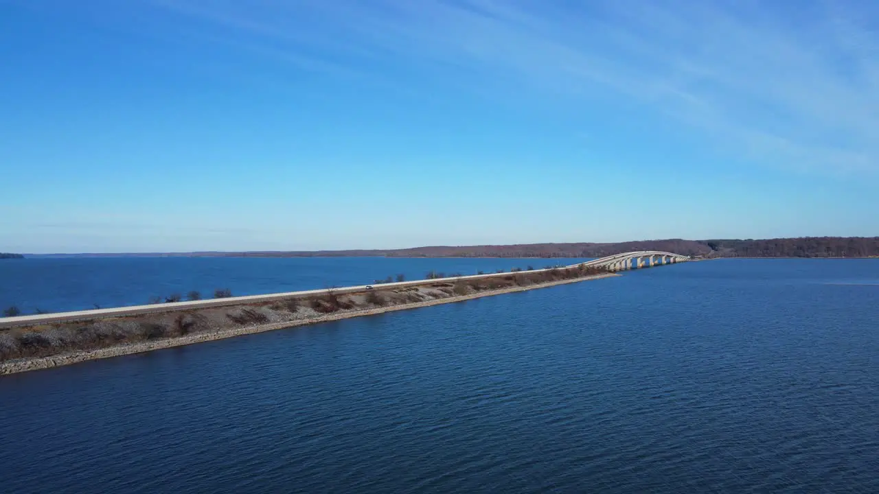 Aerial rise of a bridge rising over a blue lake with blue skies