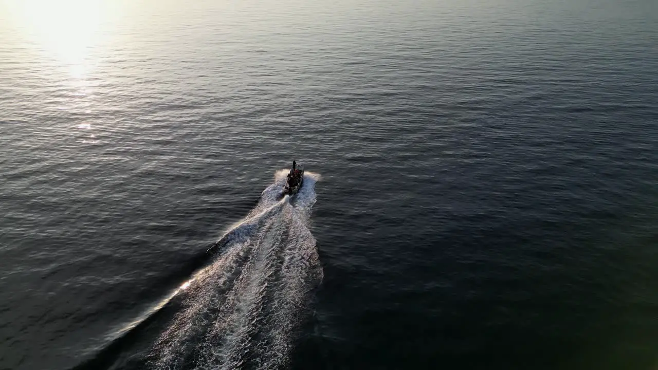 Drone aerial view of a small speedboat cruising on the ocean during sunset