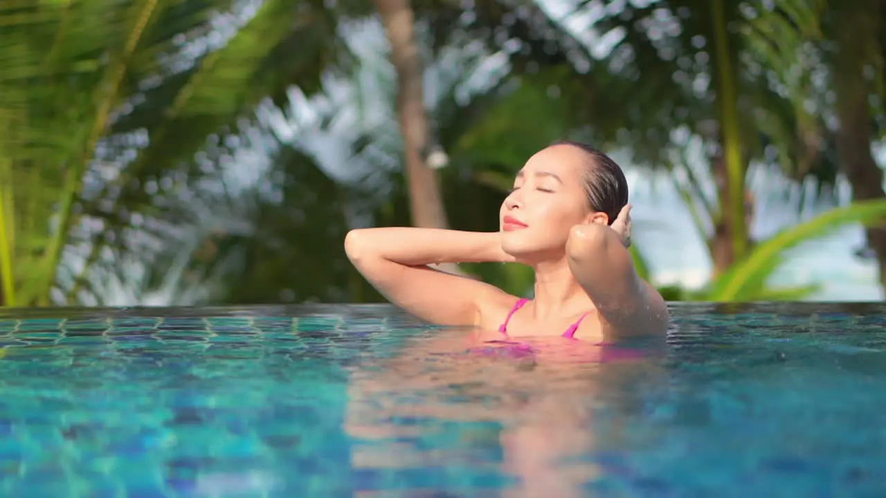 Young woman strokes her wet hair in pool