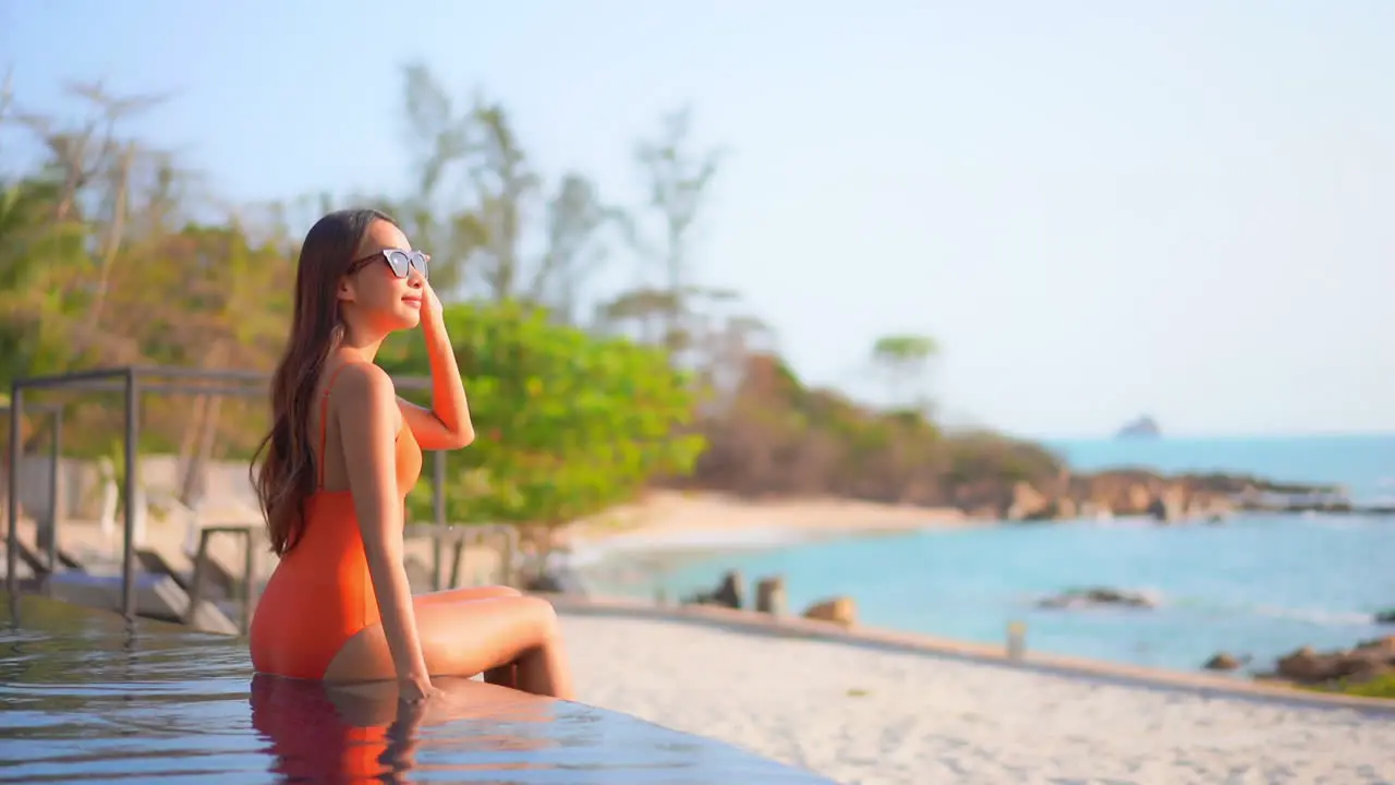 A young woman sitting on the edge of a swimming pool as she looks out over the beach and shoreline