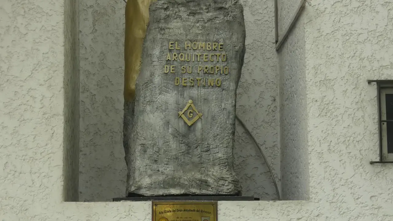 A stone monument with the masonic symbols of the square the compass and the letter G and above a phrase in Spanish translated to "Man architect of his own destiny"