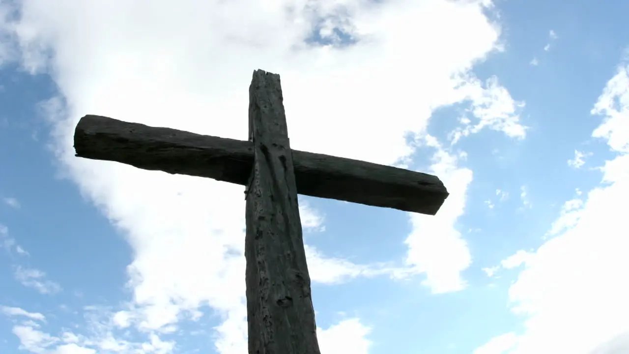 A cross in silhouette stands beneath swiftly moving clouds in a blue sky