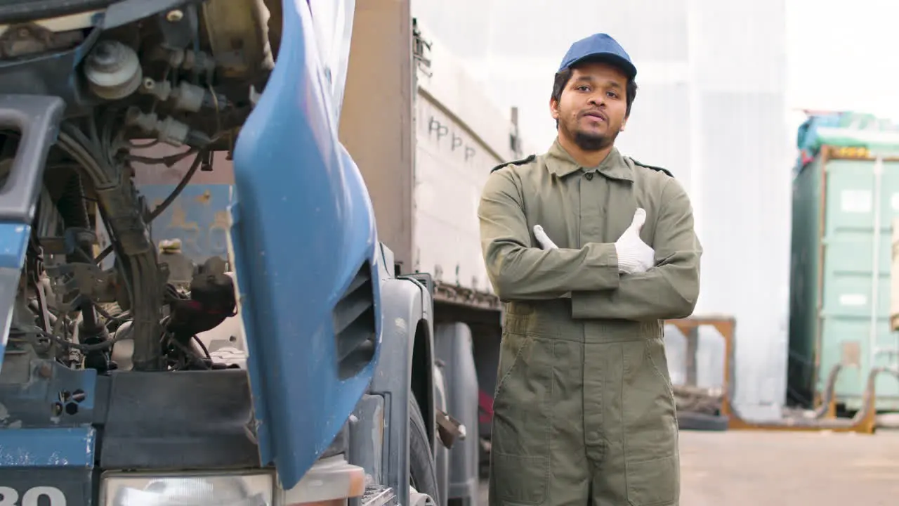 Worker Fixing A Truck In A Logistics Park Then Looks At The Camera With Crossed Arms