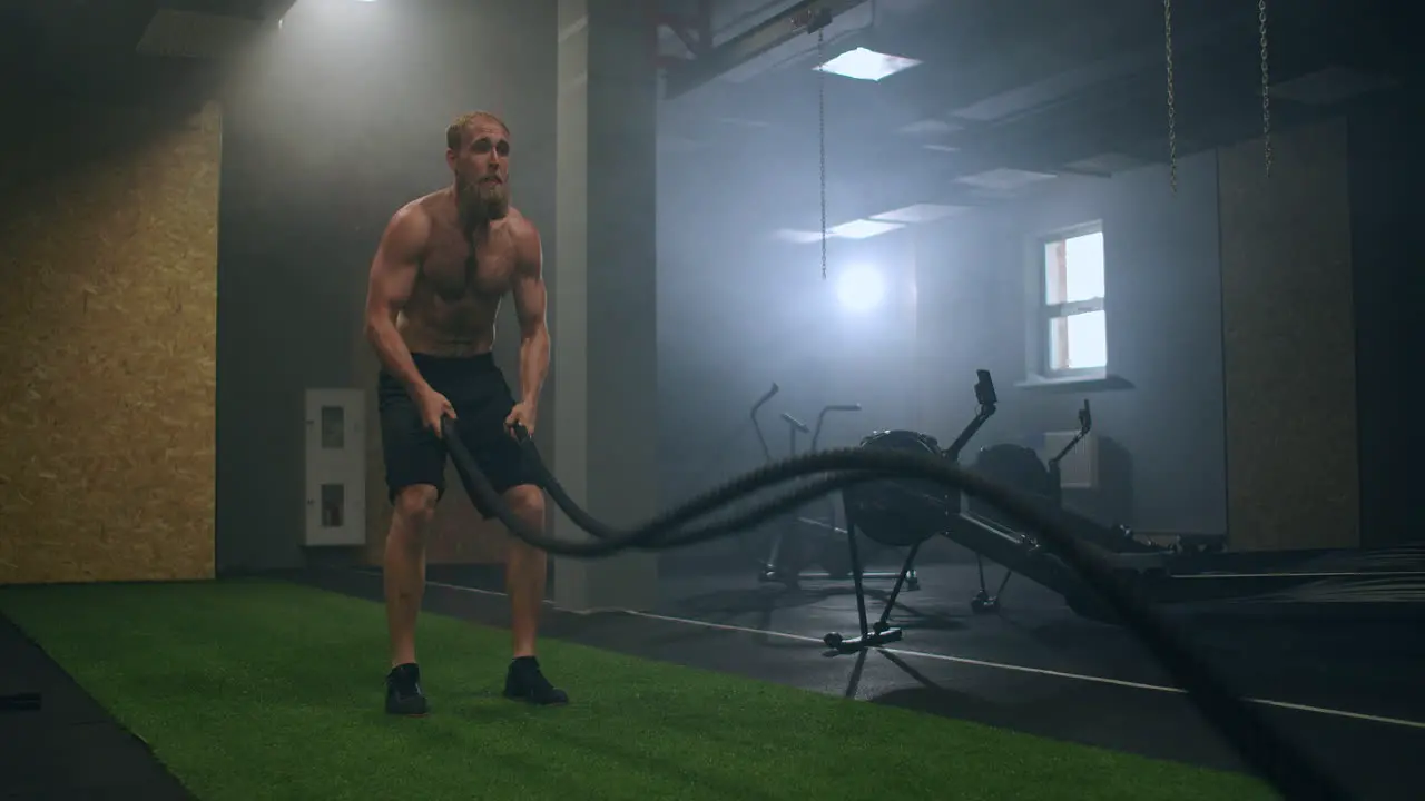 Fitness man exercising with battle rope abandoned warehouse Tough man working out in cross training gym made inside old factory