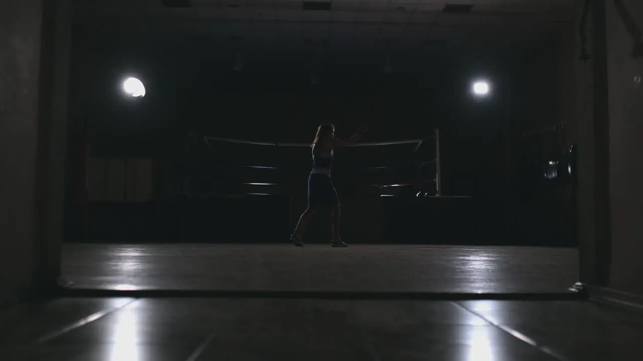 Professional beautiful female boxer otbryvatyvat blows conducting a fight with a shadow in a dark hall of the hall in slow motion in blue clothes and red bandages on her wrists zoom camera steadicam shot