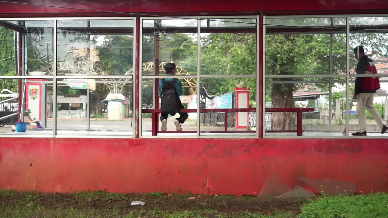 Static shot of male Student sitting at bus stop and waiting for bus during Cleaning Service cleans the floor outdoors