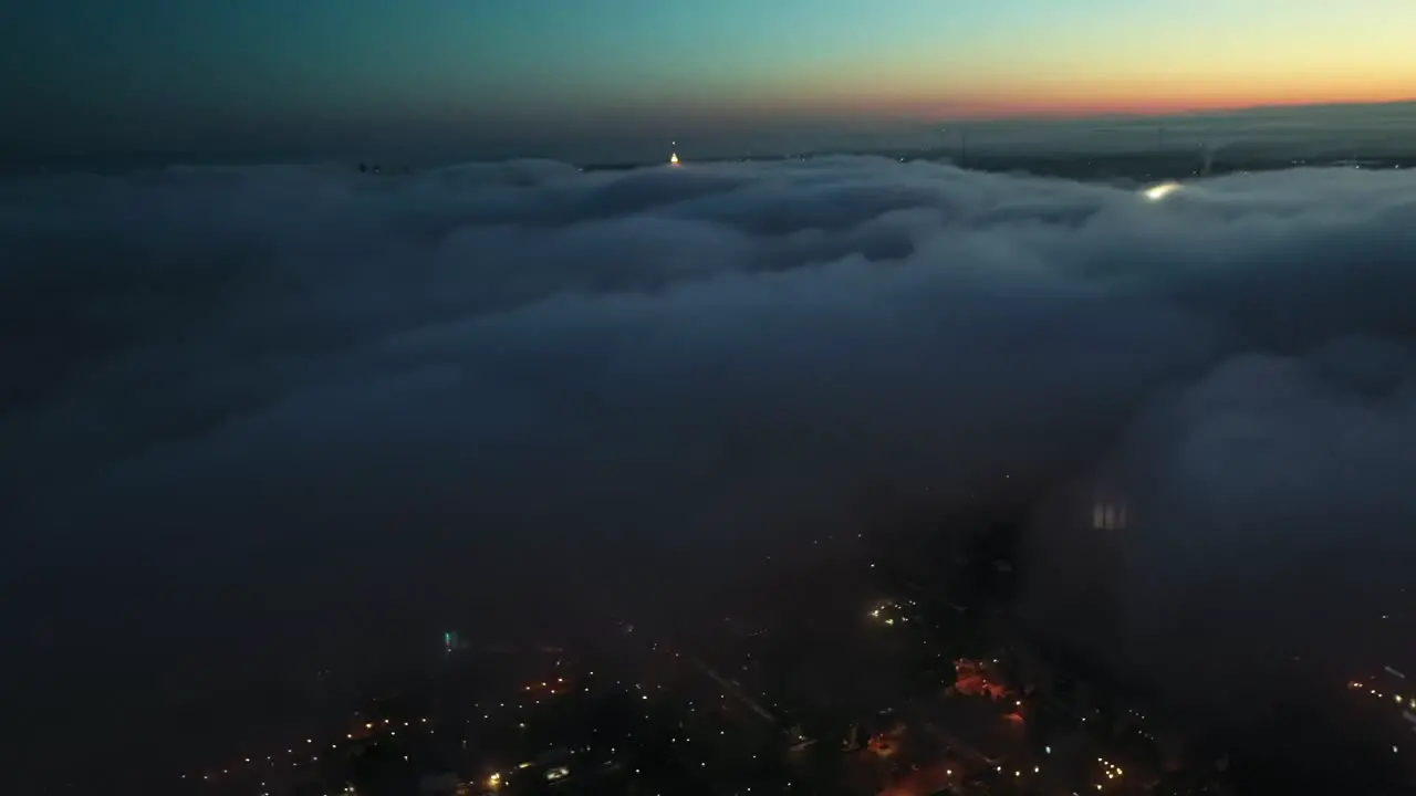 Aerial birds eye shot over dark cloudscape and illuminated city on the valley at sunrise time