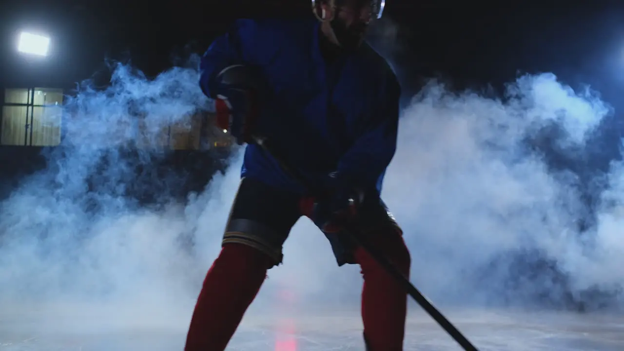 Male hockey player with a puck on the ice arena shows dribbling moving directly into the camera and looking directly into the camera against a dark background in the smoke