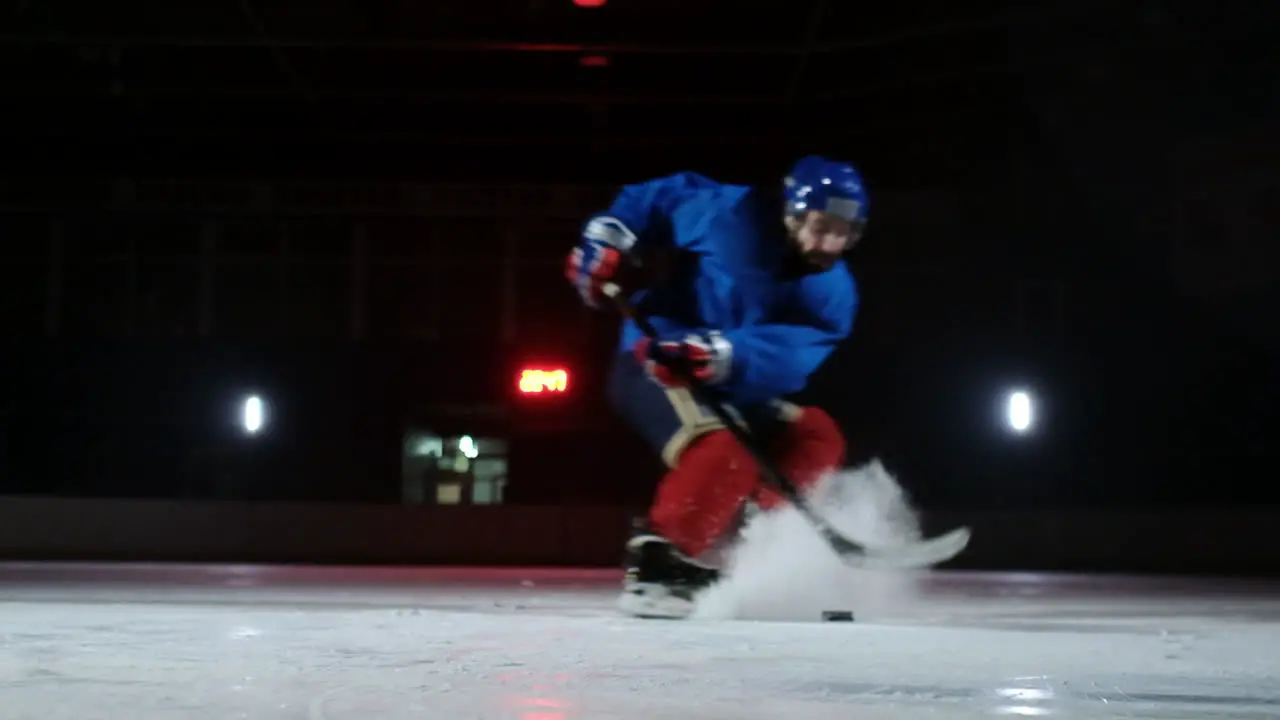 Close-up of the puck is on the ice and in slow motion hockey player pulls up and the snow flies into the camera and he takes the puck stick