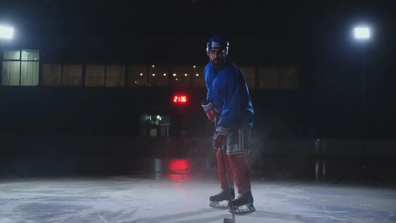 Man hockey player in hockey uniform leaves with a stick in his hands out of the darkness and looks straight into the camera