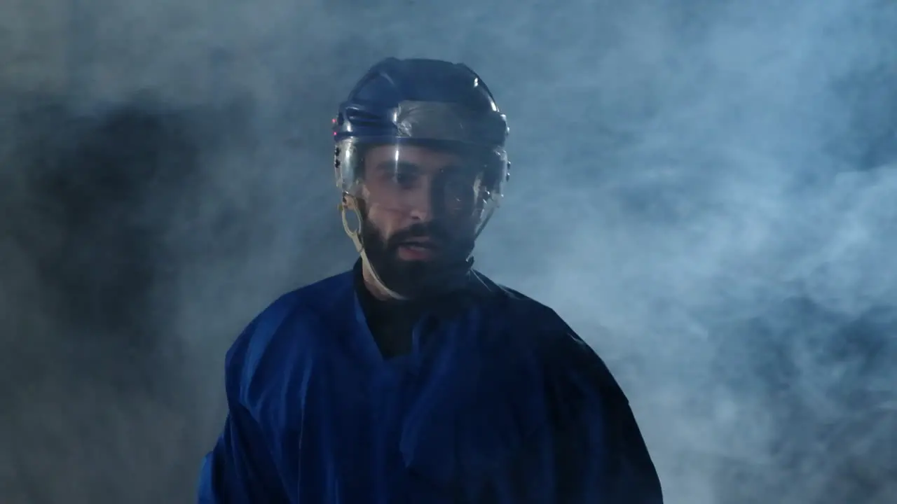 Professional hockey player with a stick and a puck moves on Luda in skates and helmet on a dark background and smoke Dribbling with the puck of a young man on the ice arena