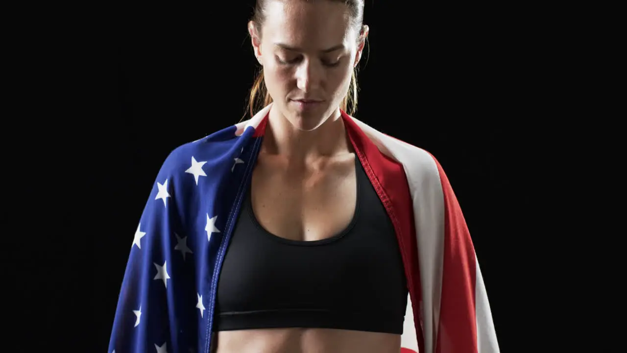 Young Caucasian athlete woman draped in an American flag on a black background