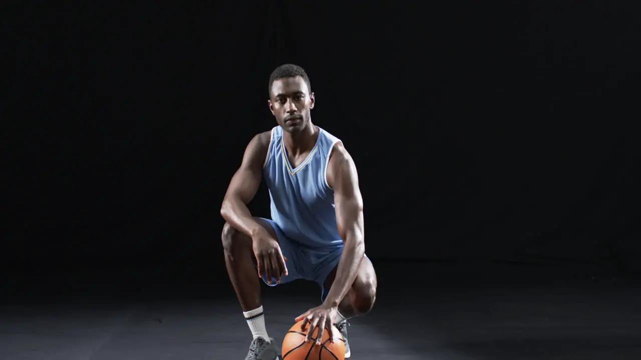 African American man poses confidently on a basketball court with a black background