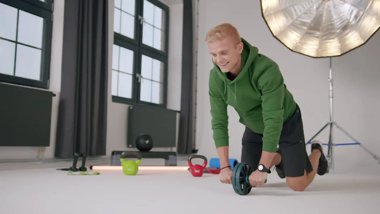 Young caucasian male on knees working out on floor with ab roller