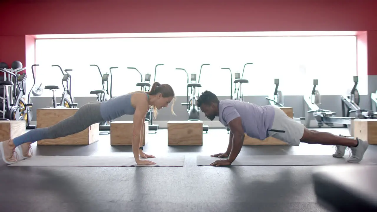 Fit young Caucasian woman and African American man perform planks at the gym