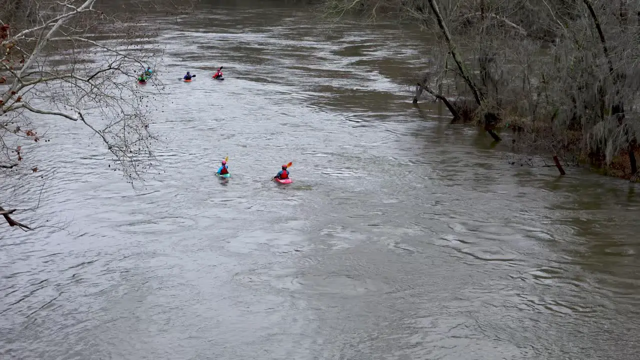 A group of kayakers navigating a muddy river during the winter on an overcast day