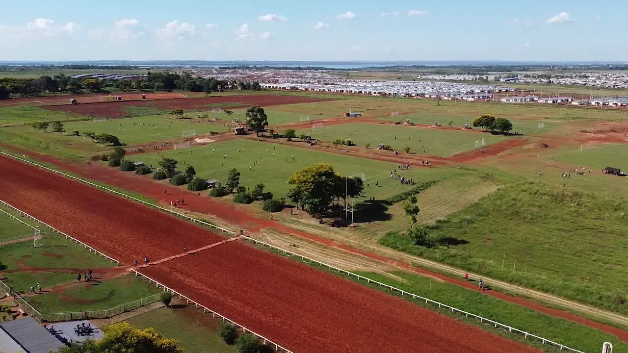 Drone strafe past football kids playing football on many football pitches sunny blue sky