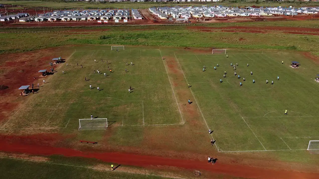 Drone slow strafe past two football games with active play and buildings in the background Posadas hipodrome