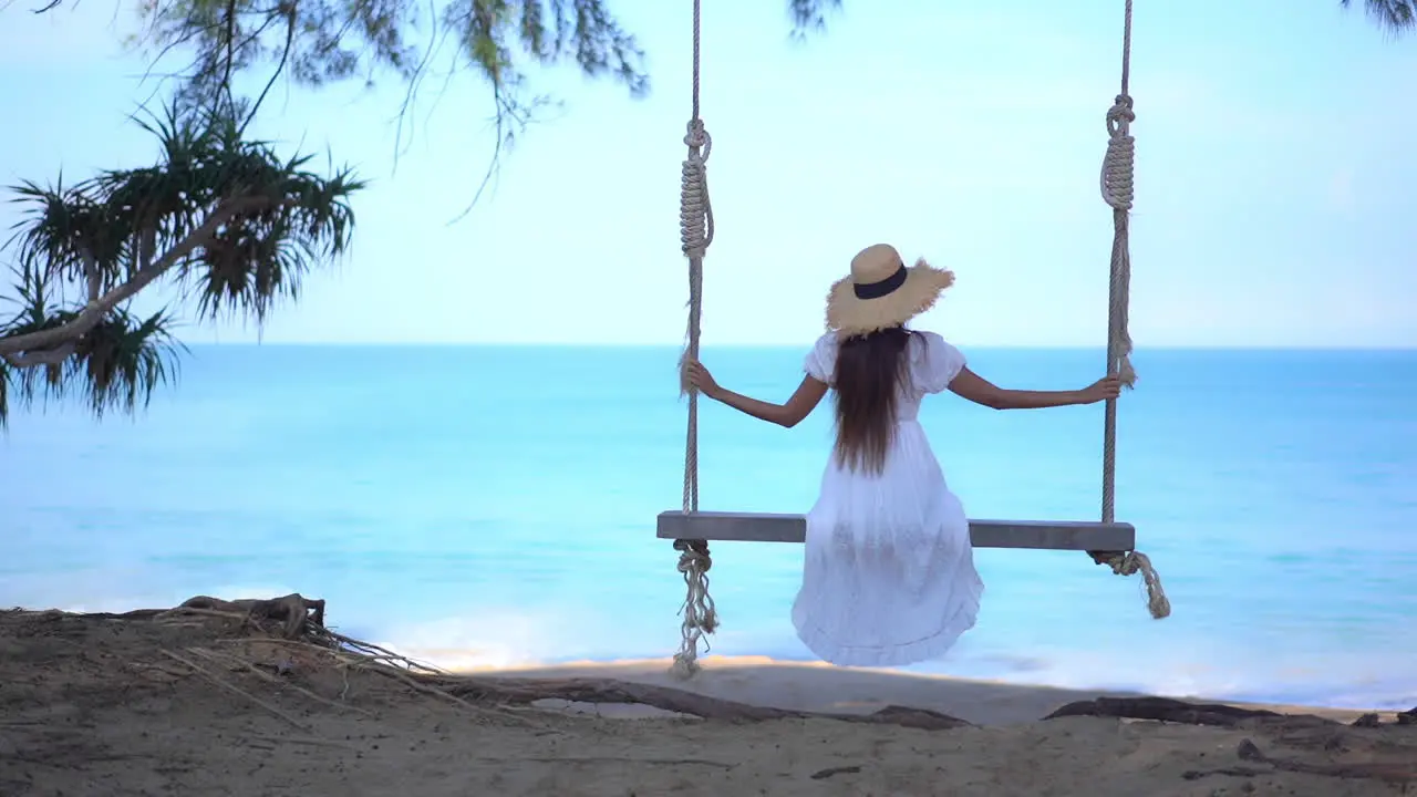 Back of Woman in White Summer Dress on Sing Under Tree With Stunning View of Tropical Sea