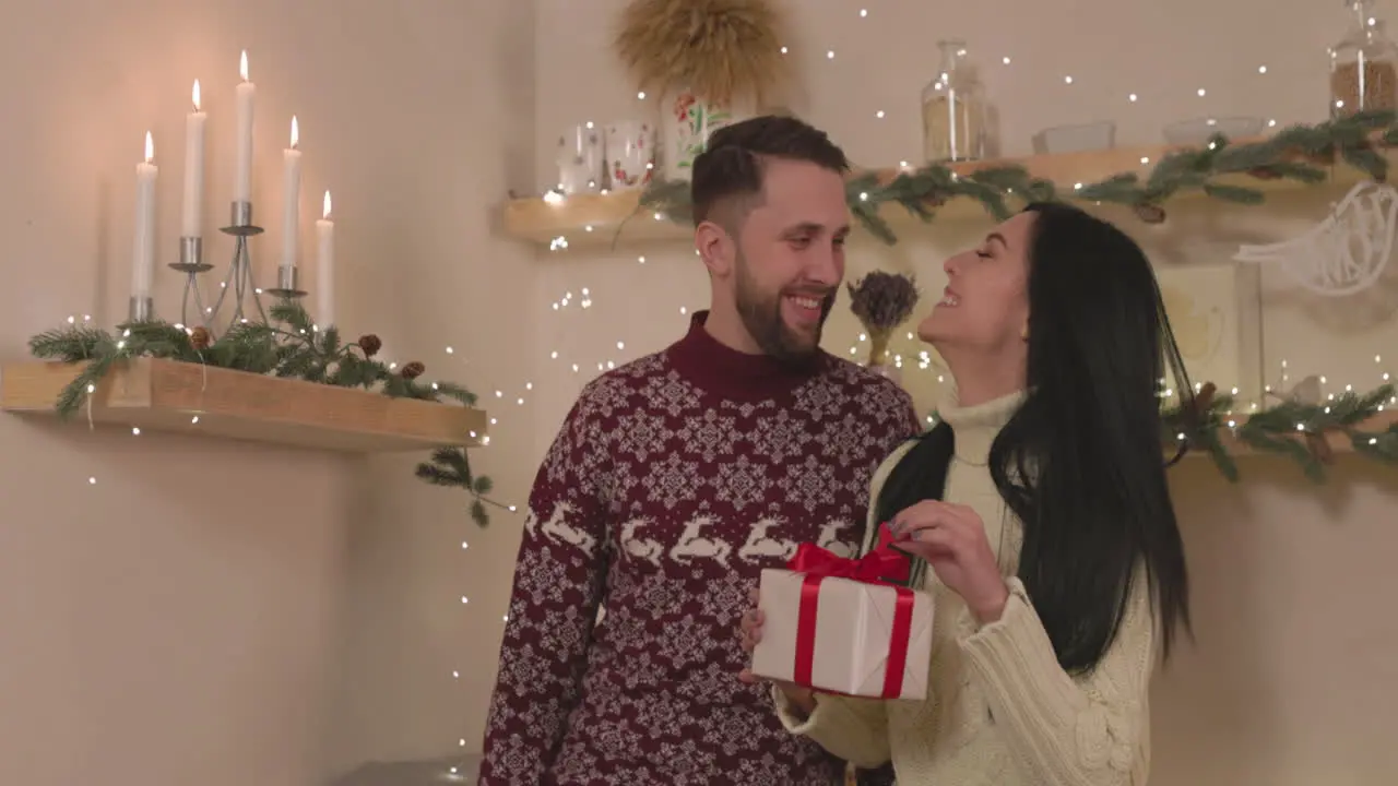 Happy Woman Holding A Christmas Gift Box And Kissing Her Boyfriend At Home