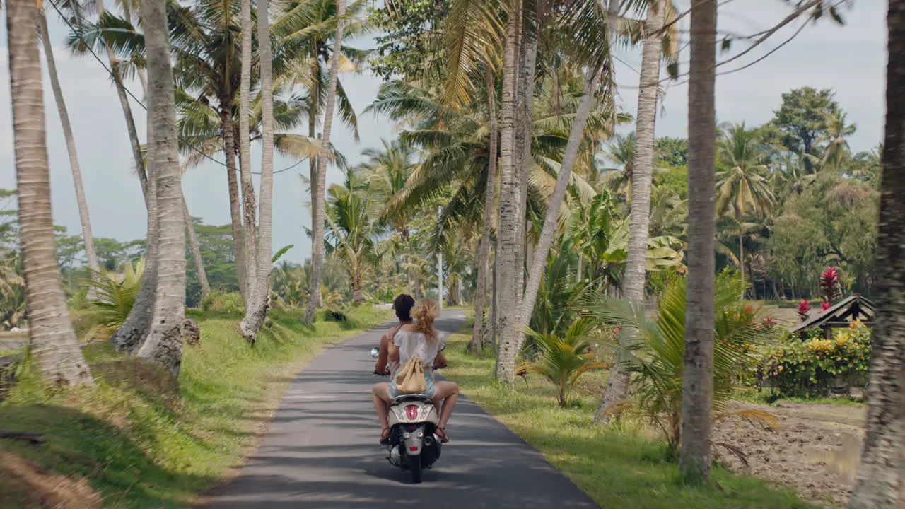 tourist couple riding motorbike on tropical island happy woman celebrating freedom with arms raised enjoying vacation road trip with boyfriend on motorcycle ride rear view