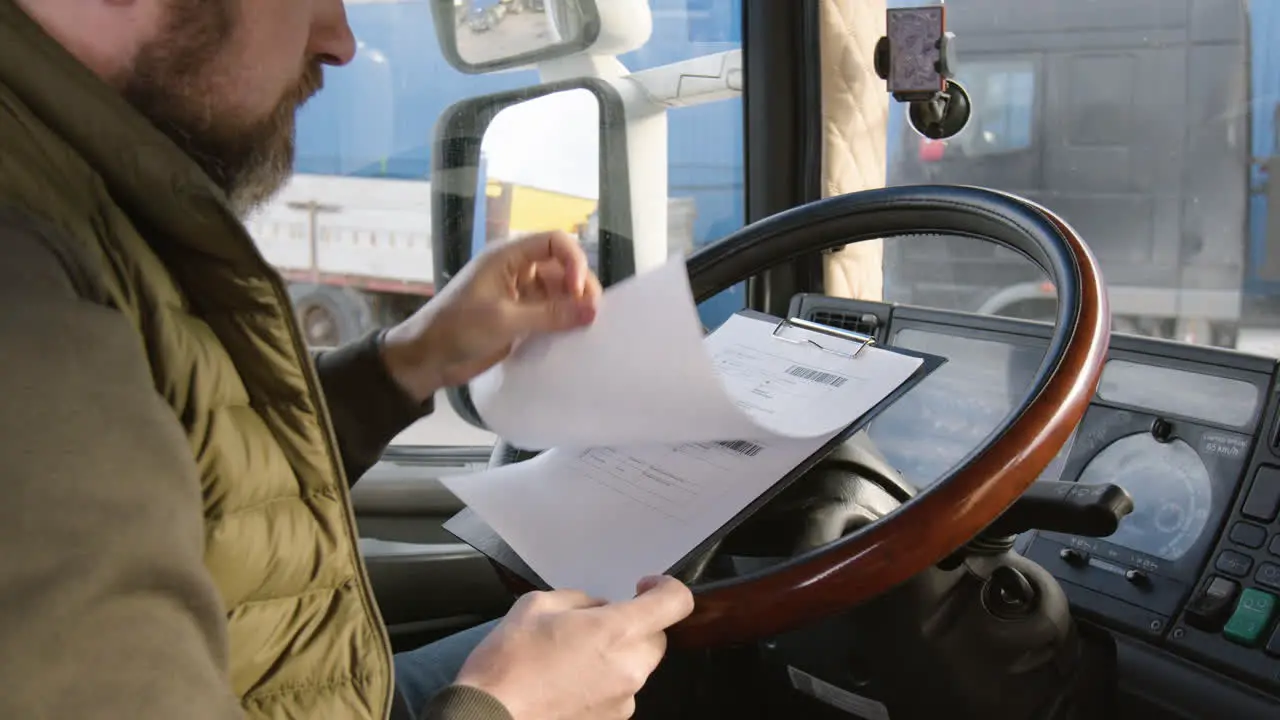 Rear View Of Worker Sitting In A Truck In A Logistics Park While Reading Documents