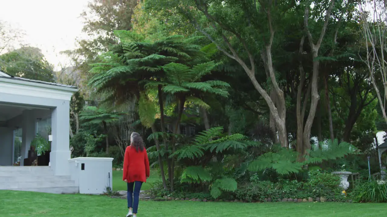 Rear view of senior caucasian woman walking through garden towards terrace