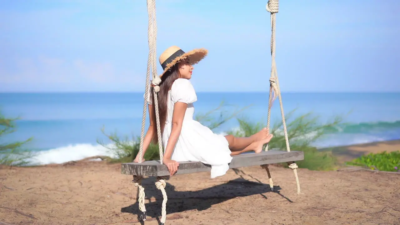 Exotic Woman in White Summer Dress on Wooden Swing by Tropical Beach on Sunny Day Full Frame