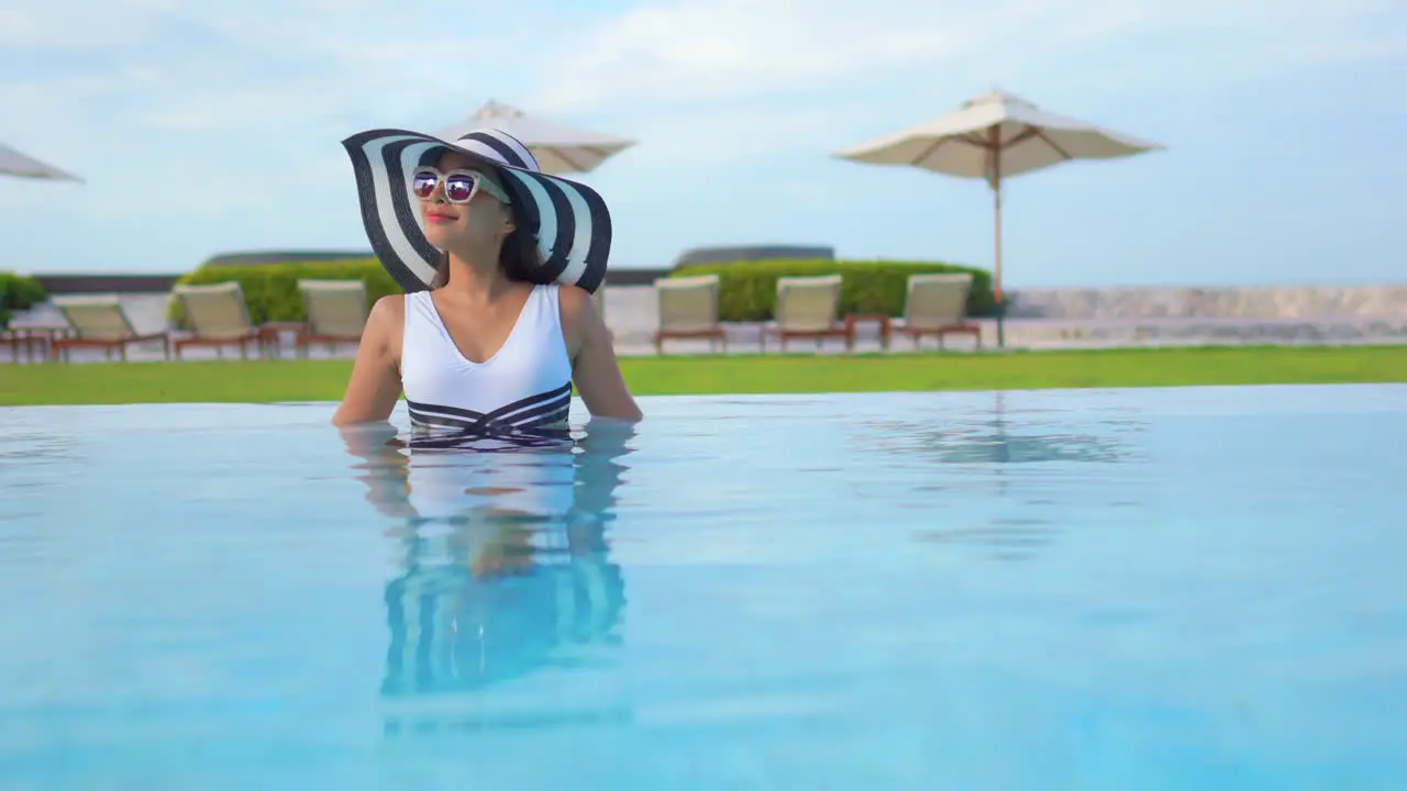 Satisfied Remarkable Asian Woman in Pool of Luxury Resort With Summer Hat and Sunglasses Static Shot Copy Space