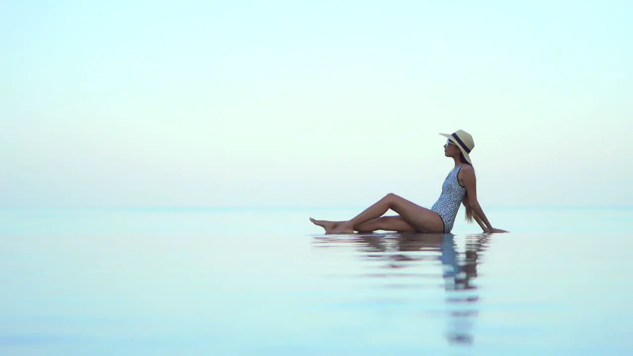 Classy Woman in Swimsuit and Hat on Infinity Pool Poolside With Heavenly Skyline Enjoying in View