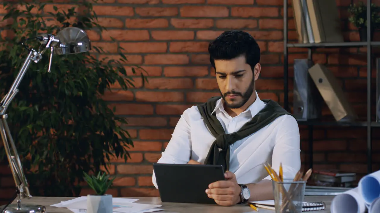 Young Arabian Businessman Scrolling And Taping On The Tablet While Sitting In The Modern Office