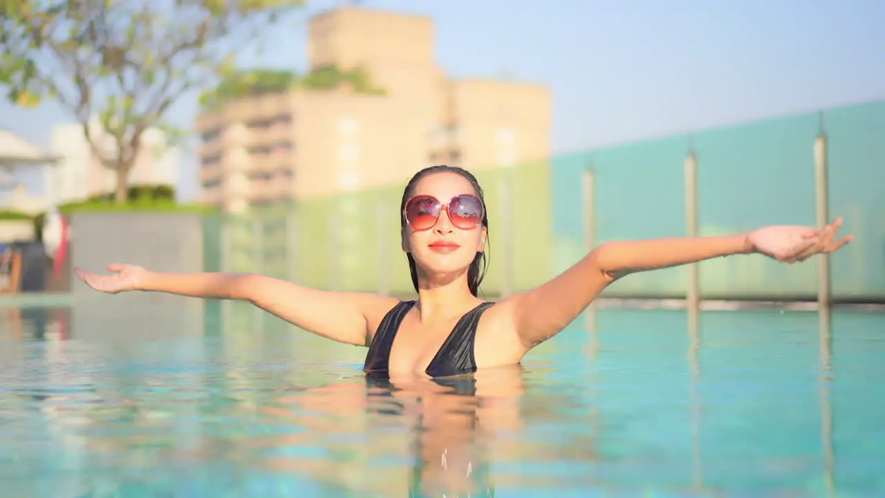 A beautiful woman in a resort swimming pool raises her arms in greeting the morning