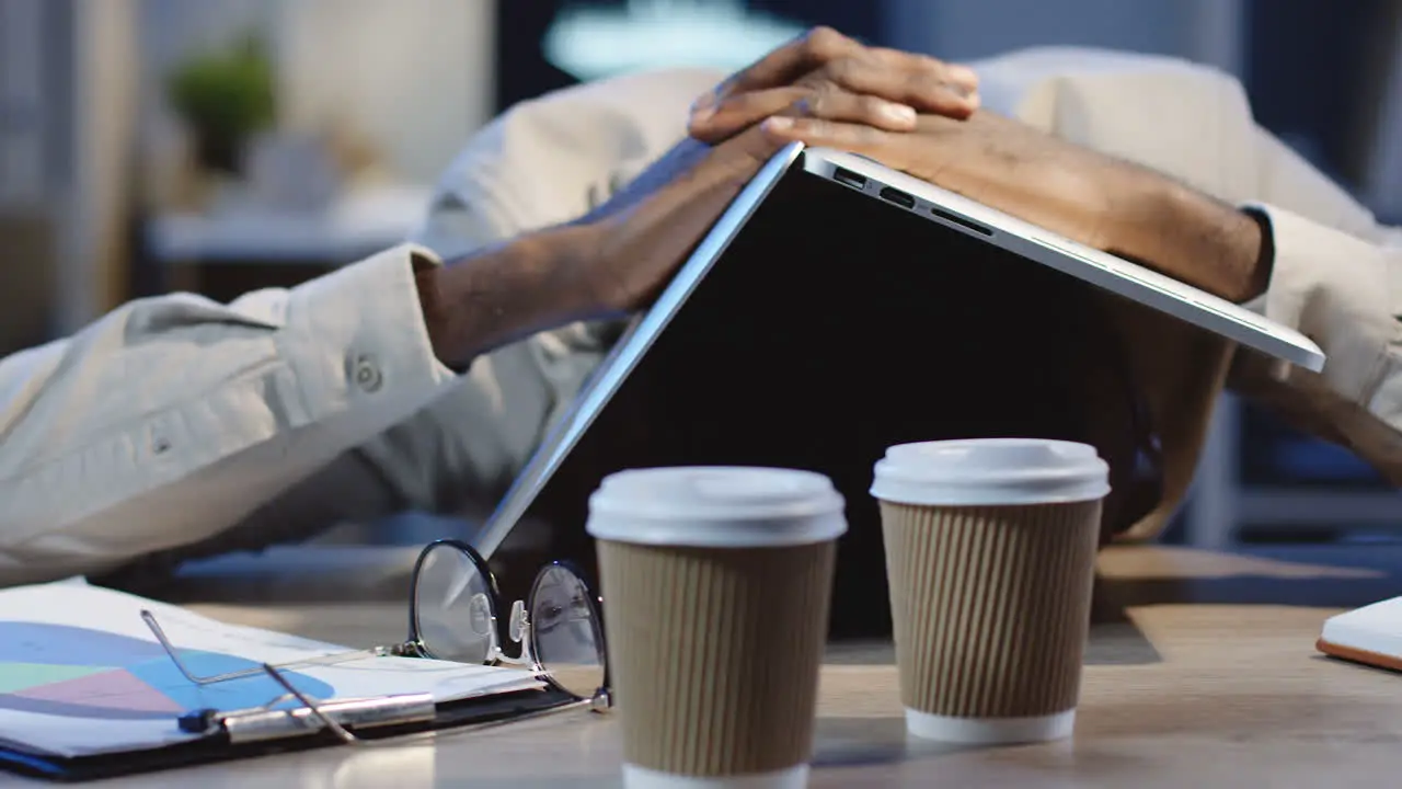 Close Up View Of Tired Office Worker Sleeping On The Table With Laptop Over Head In The Office At Night