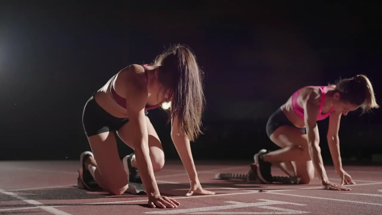 Eine Reihe Läuferinnen Hockt In Der Startposition Bevor Sie Mit Dem Rennen Beginnen Frauen Starten Mit Laufschuhen Im Stadion Von Der Startlinie Im Dunkeln Mit Scheinwerfern In Zeitlupe