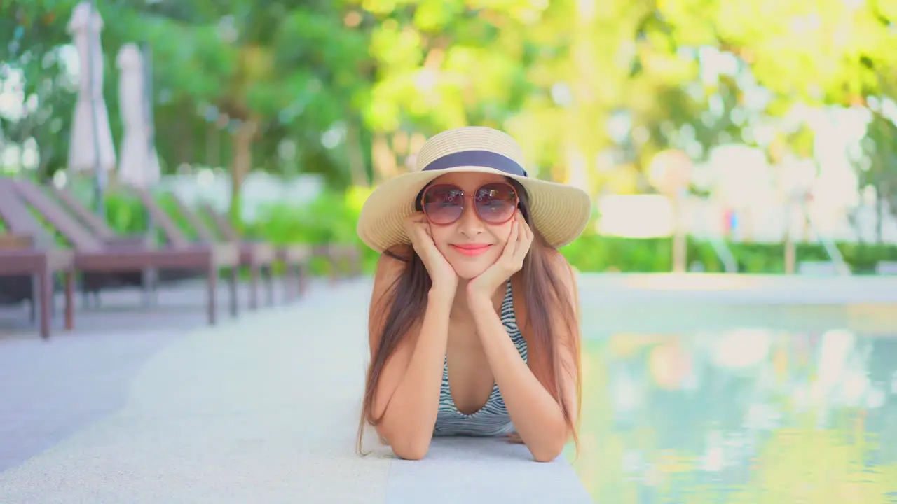 Beautiful woman laying on her belly next to hotel swimming pool looking into the camera