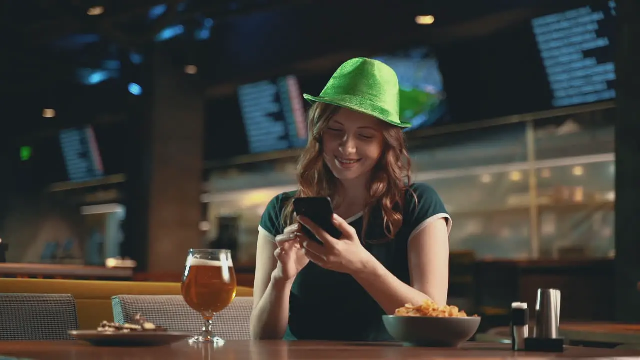 Mujer Muy Joven Usando Un Teléfono Inteligente Bebiendo Cerveza Y Usando Un Sombrero Verde Irlandés