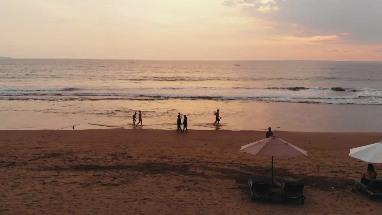 Slow motion aerial footage of people walking at the beach during sunset