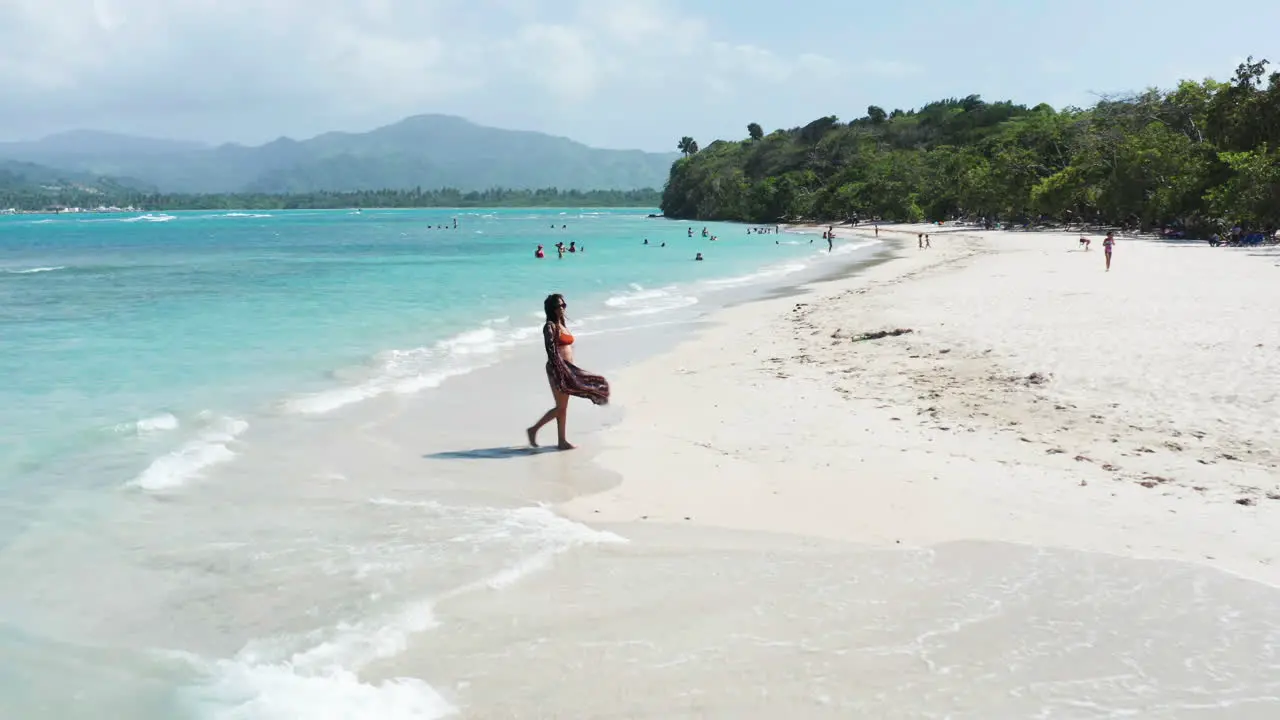 Young woman strolls on beach showcasing pristine Caribbean waters aerial dolly forward