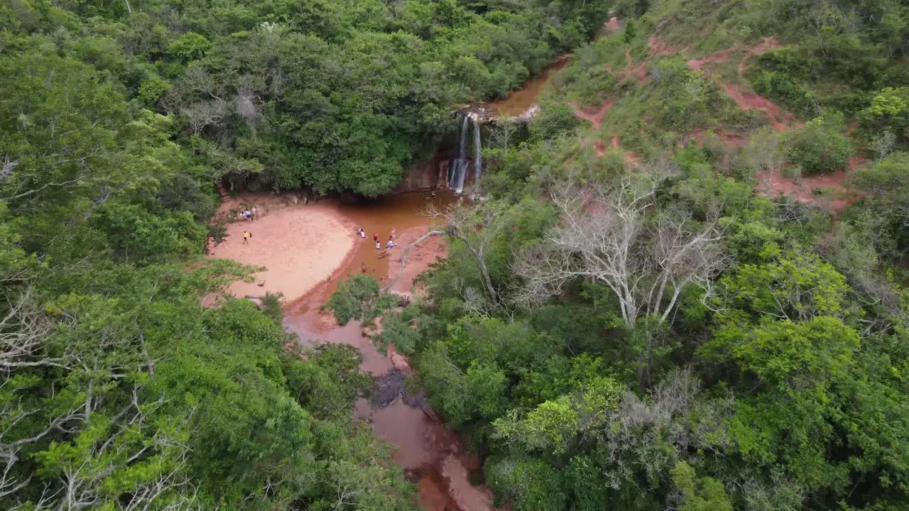 Aerial descends to picturesque waterfall in jungle people swimming