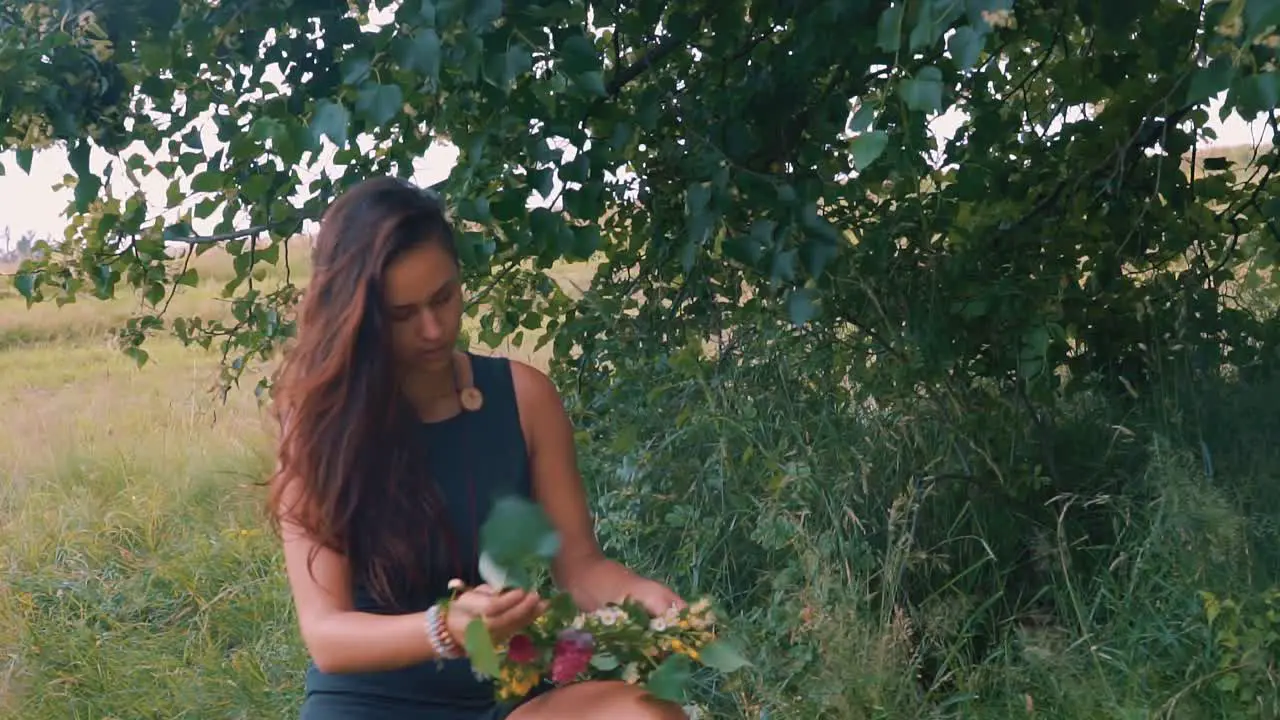 A beautiful young girl wearing black dress and arranging flowers and leaves around the tree in outdoors during visit to fields