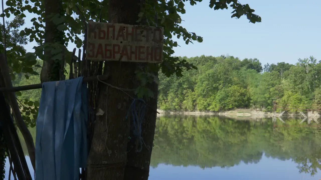 Sign nailed to tree reads swimming not allowed at Bulgarian fishing lake