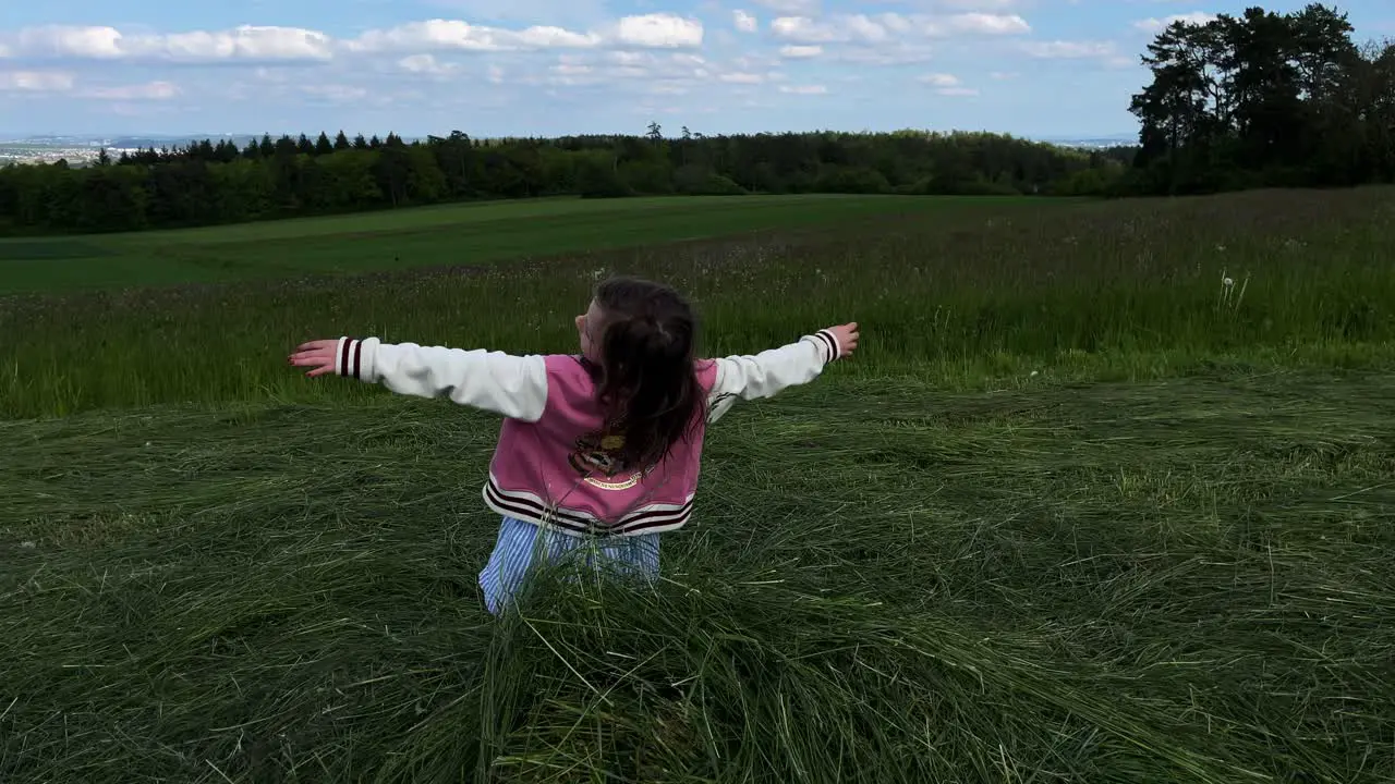 A young little girl playing and falls on her back onto a pile of mowed grass in a field