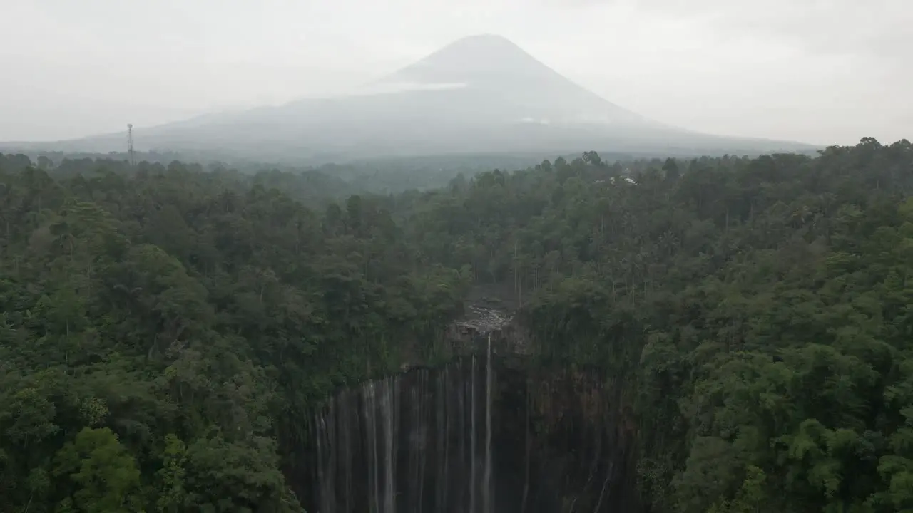 Aerial Tumpak Sewu waterfall in Java jungle volcano cone in distance