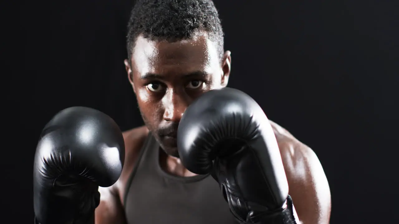 Focused African American boxer training in a dark gym on a black background