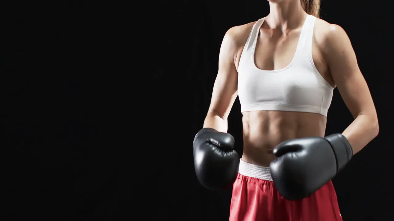 Young Caucasian woman boxer in boxing gear poses confidently on a black background