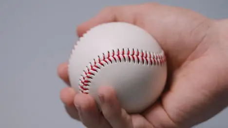 Close Up Shot Of Hand Holding Baseball Ball Against Grey Background