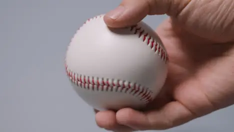 Close Up Shot Of Hand Holding Baseball Ball Against Grey Background 1