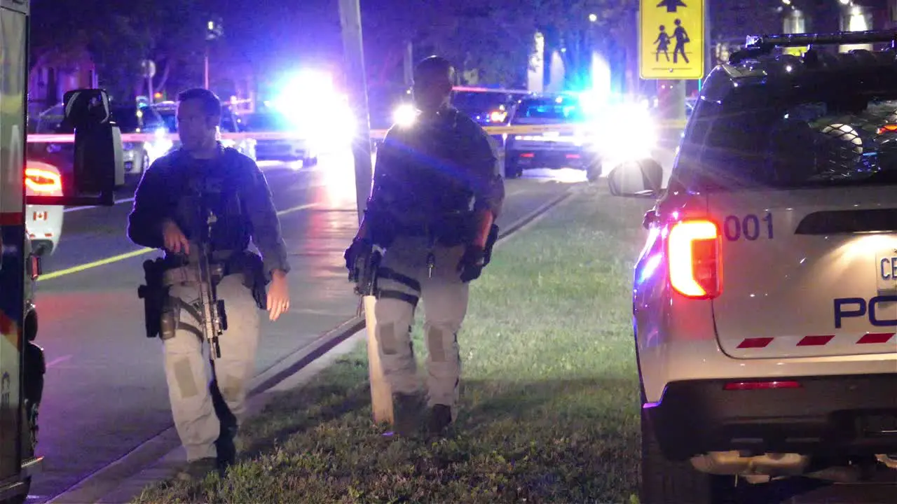 Armed police officers in yellow taped crime scene with flashing emergency lights