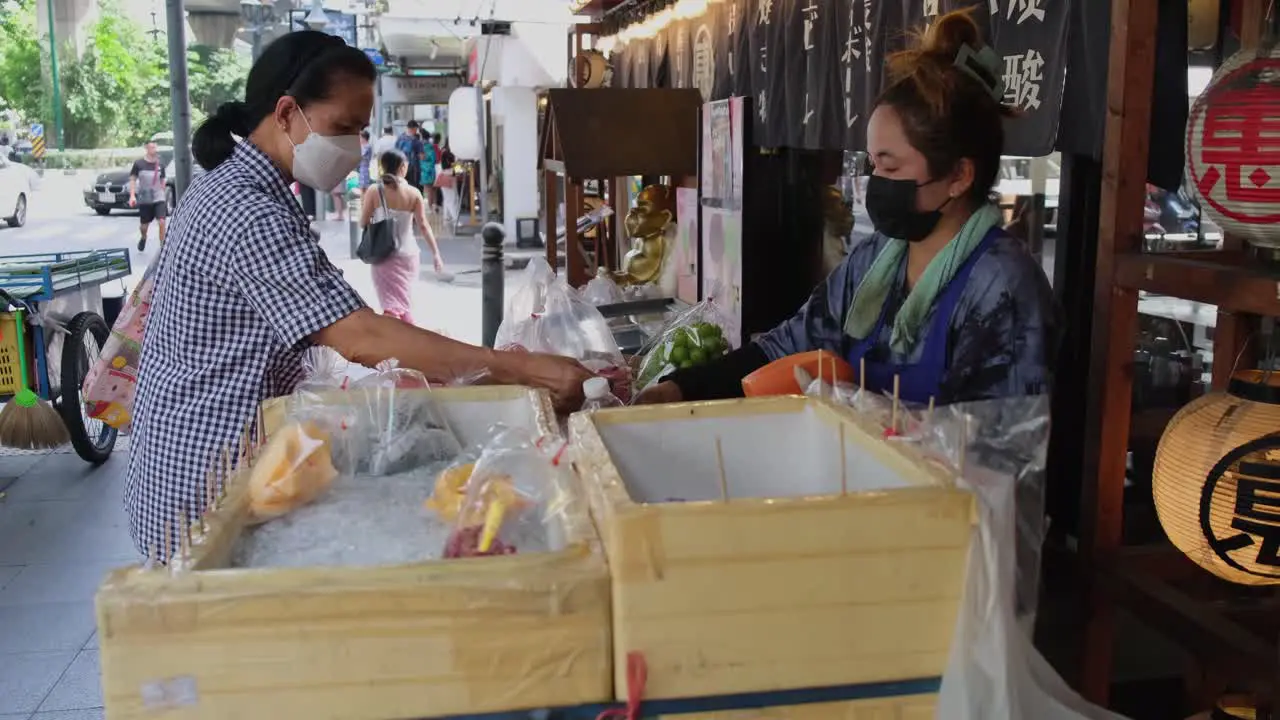 Woman pays the fruit vendor then takes more to buy Street Food along Sukhumvit Road in Bangkok Thailand